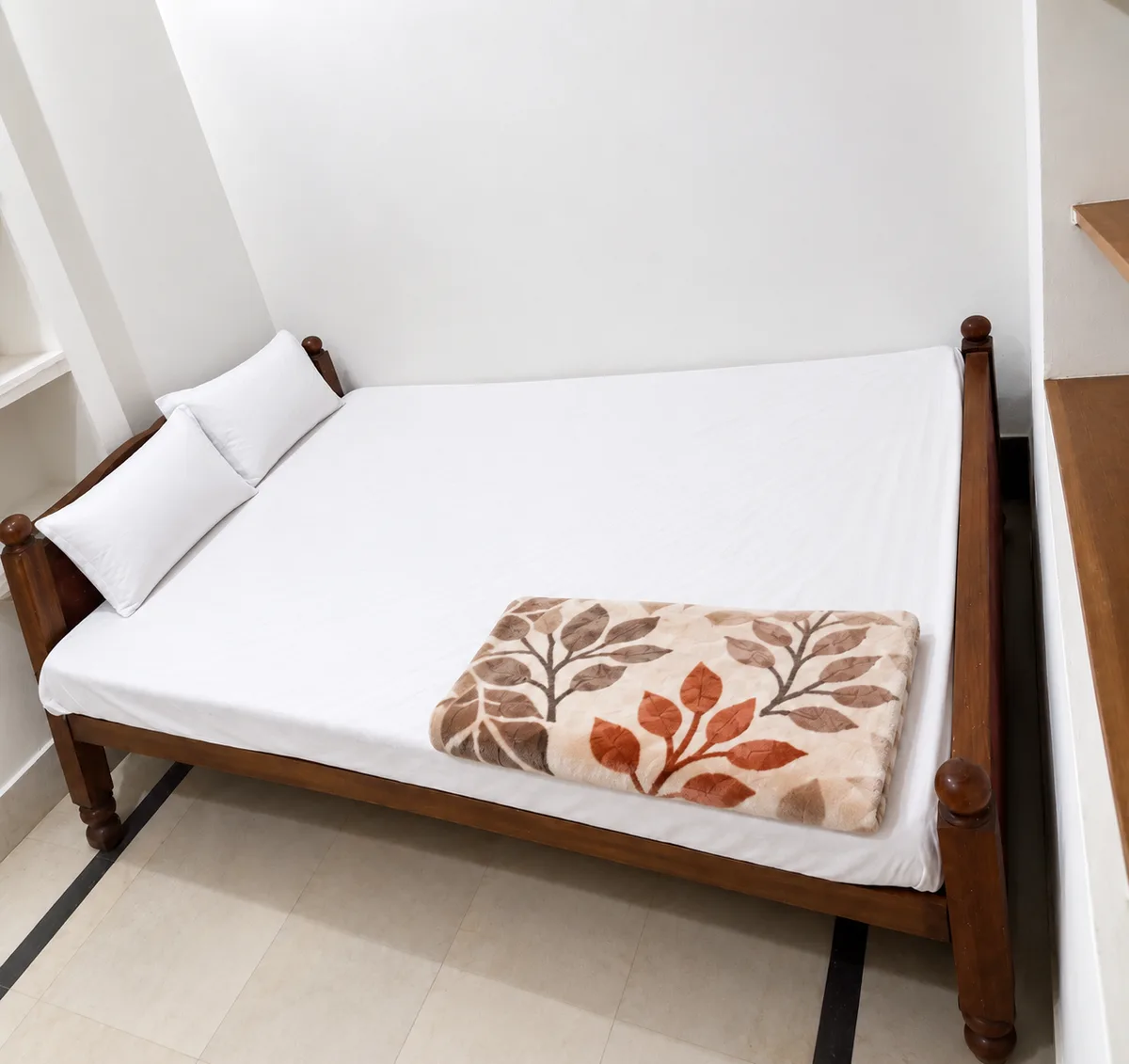 A guest room at Bharat Bhawan, Gaya — wooden bed with white sheets and a blanket, tiled floor